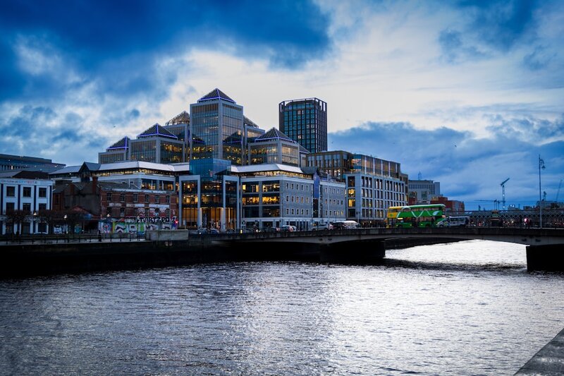 Modern office buildings along a river in Dublin's docklands under a cloudy sky