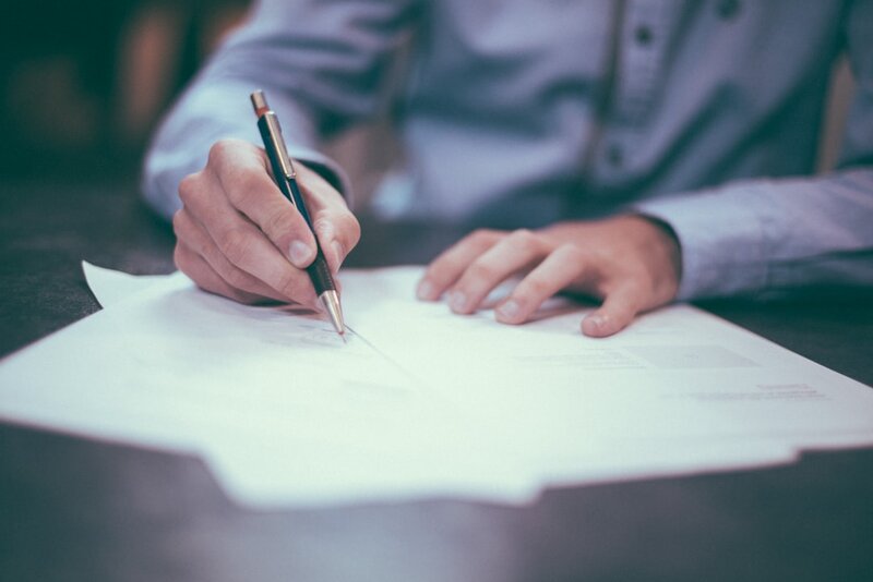 A person signing a contract at a desk, representing NIS2 supply chain security obligations arriving through customer contracts