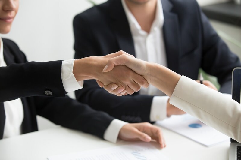Two people shaking hands in front of a laptop, representing a software project handover
