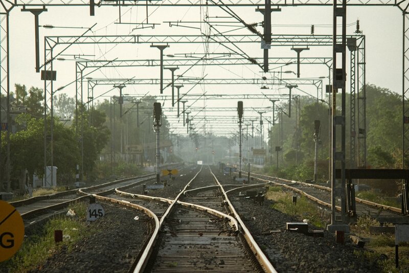 Multiple train tracks converging at a junction with signals overhead, representing an AI model routing layer