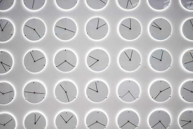 A white wall covered with many clocks showing different time zones