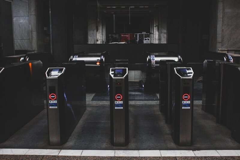 A row of black metal turnstiles controlling entry to a building