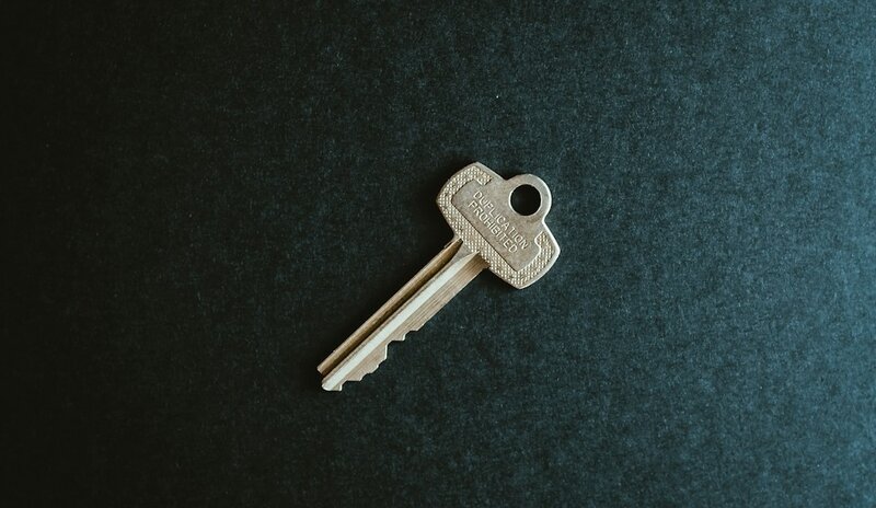 A brass door key stamped with the words Duplication Prohibited, on a dark background
