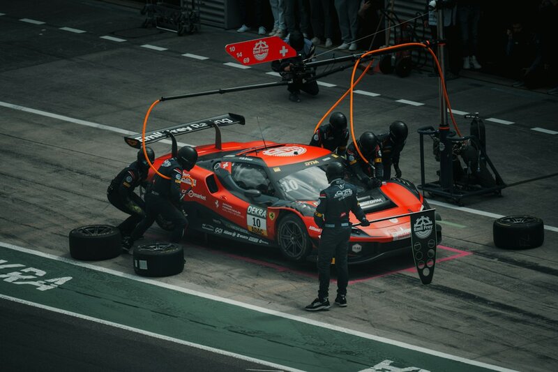 A pit crew of seven surrounding a stationary racing car in the pit lane