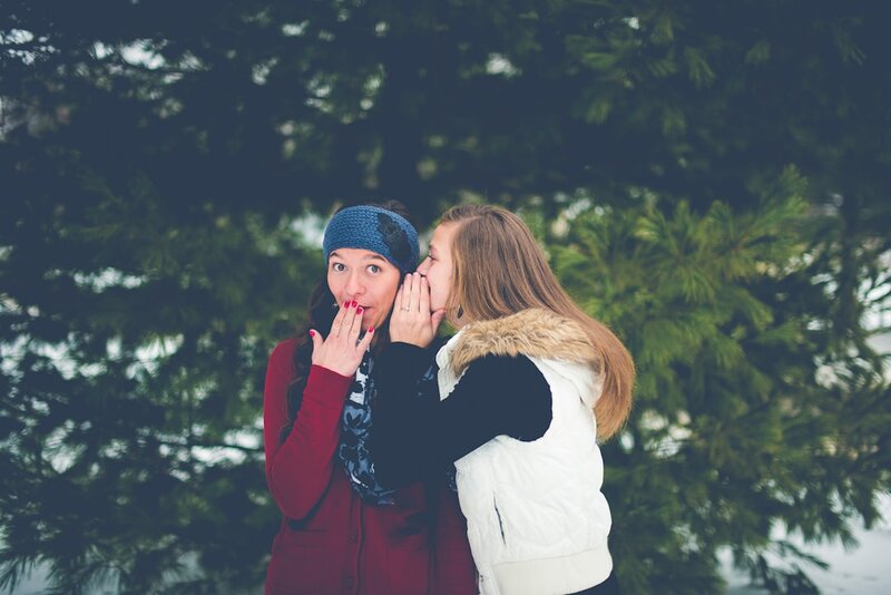 One woman whispering into another woman's ear, hand cupped over her mouth