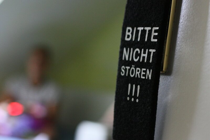 A 'bitte nicht stoeren' do not disturb sign hanging on a door handle, with the door standing open and a person visible in the room behind it