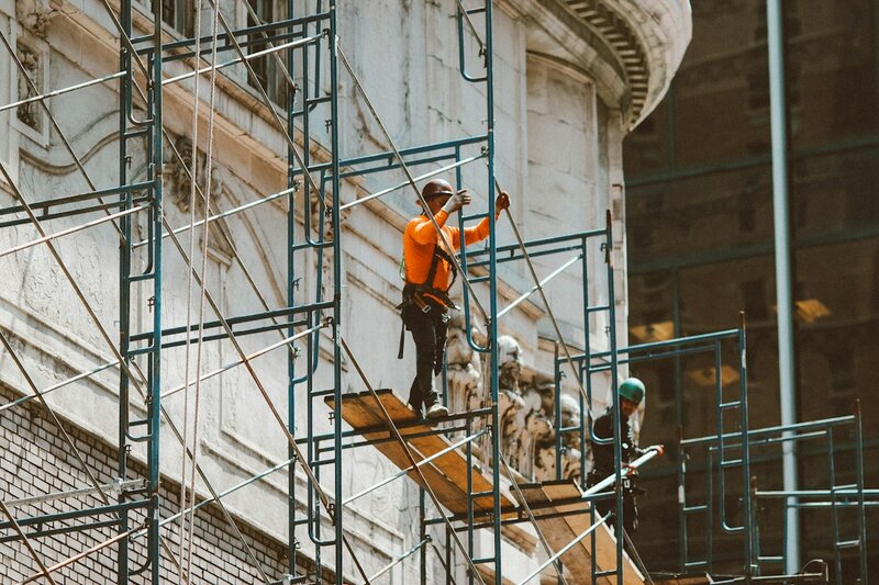Workers on scaffolding against the ornate stone facade of a building that stays standing while the work goes on behind them