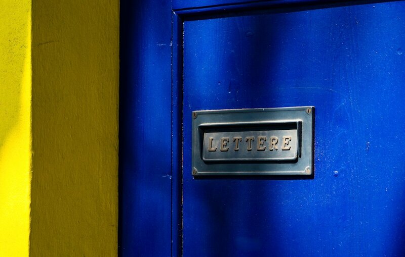 A closed blue door with a brass letter slot marked LETTERE