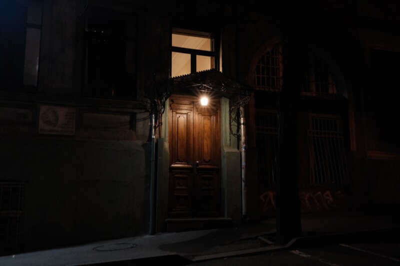 A single lamp lights the front door of a building at night while the rest of the facade stays in darkness