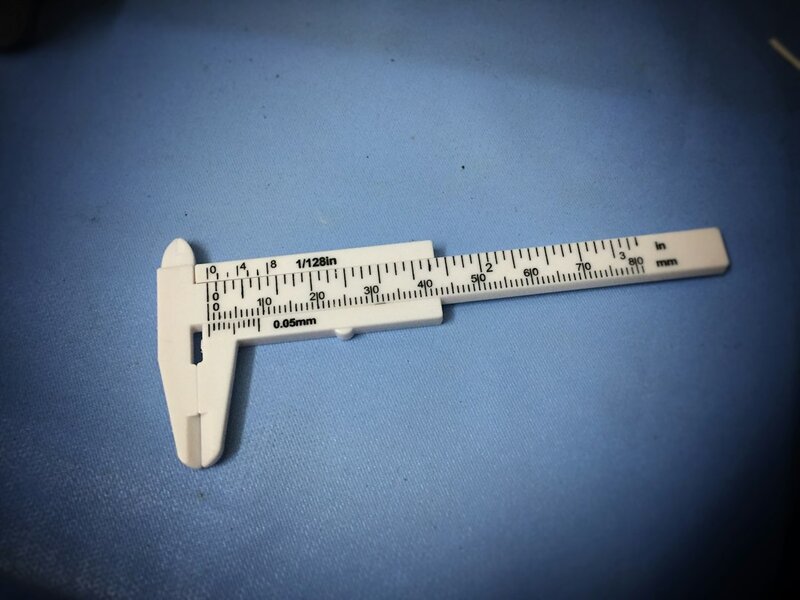 A white plastic vernier caliper on a blue cloth, its scale marked 0.05mm and 1/128in