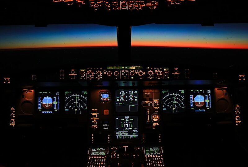 A darkened airliner cockpit at dawn, instrument panels glowing, both control columns unattended