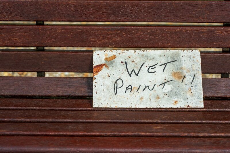 A handwritten WET PAINT sign resting on a freshly painted wooden bench