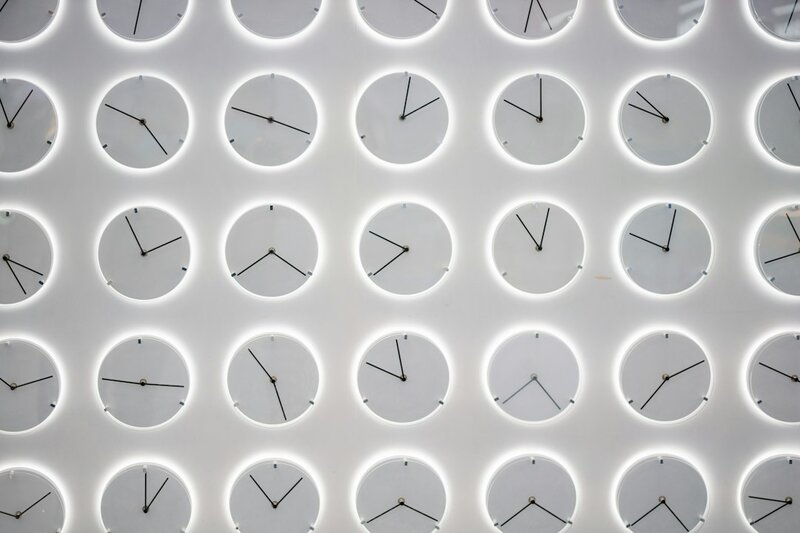 A grid of identical white wall clocks, each showing a different time, none of them labelled with a city