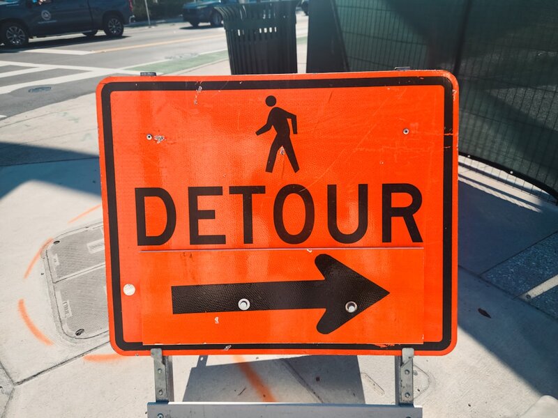 A yellow detour road sign at the side of a road
