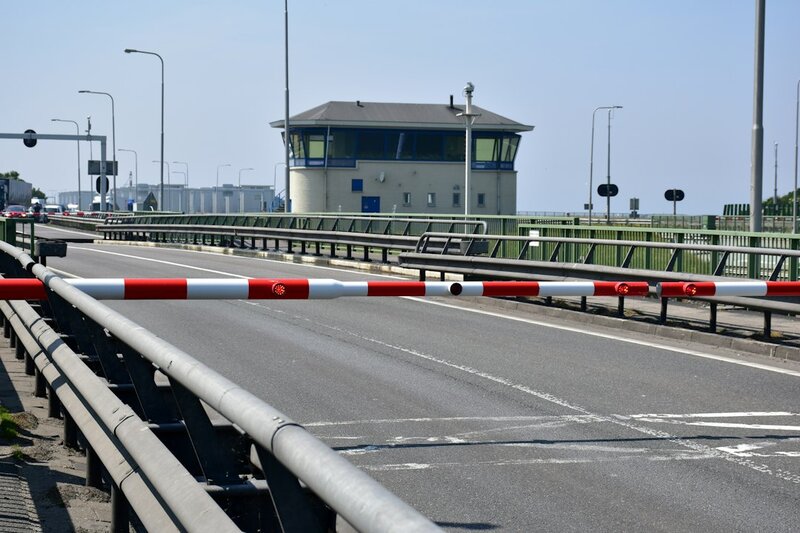 A red and white barrier lowered across an empty road, with a control tower behind it