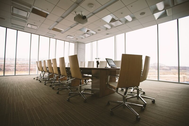 An empty oval boardroom table ringed with chairs in a glass-walled conference room