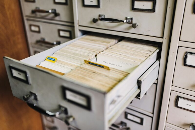 A bank of grey metal filing cabinets with one labelled drawer pulled open, full of index cards