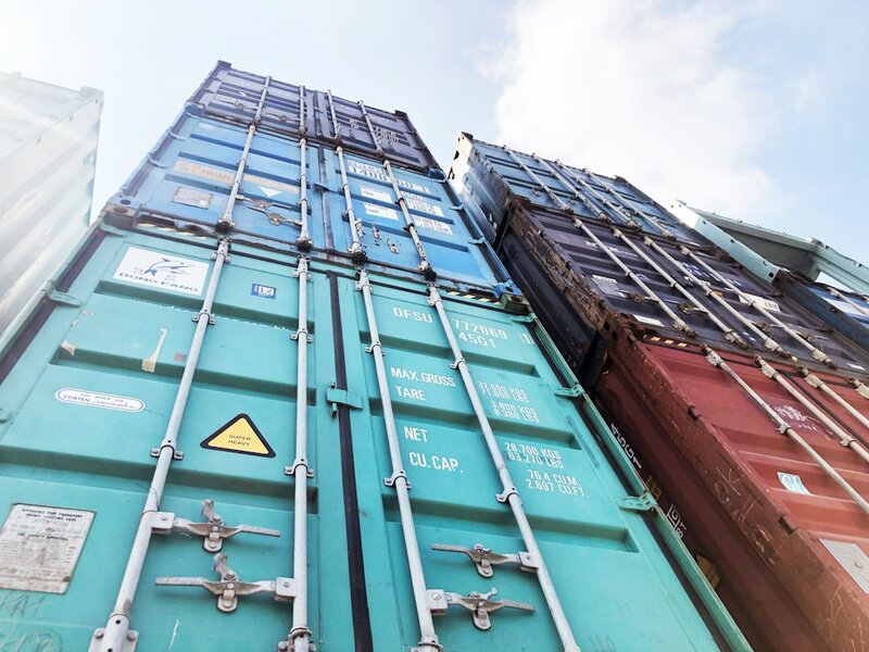Stacked shipping containers photographed from below, their doors stencilled with maximum gross weight and cubic capacity markings