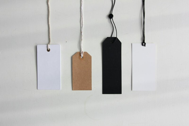 Four blank paper card tags hanging on strings against a white wall