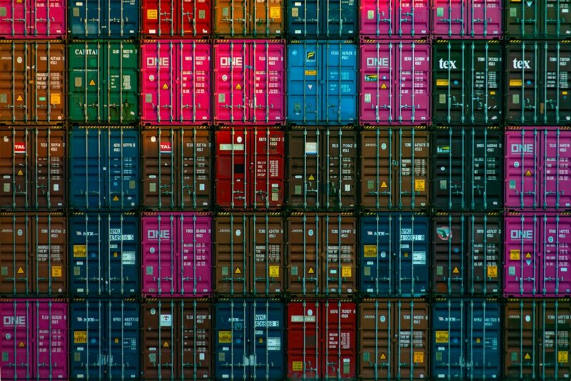 Rows of stacked shipping containers at a port, many of them identical in colour and marking